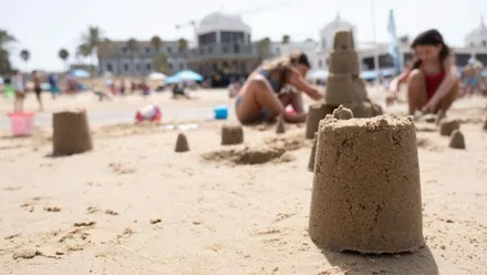 Primer plano de un castillo de arena y niñas y niños haciendo construcciones.