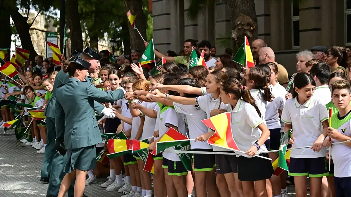 Dos agentes de la Guardia Civil saludan con el puño a un grupo numeroso de escolares que portan pequeñas banderas de España y de la Guardia Civil durante los actos celebrados en Cádiz.