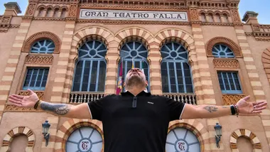 Andy aparece con los brazos abiertos ante la fachada del Gran Teatro Falla de Cádiz, con el nombre del teatro visible sobre él, en una pose similar a la del cartel de su concierto.
