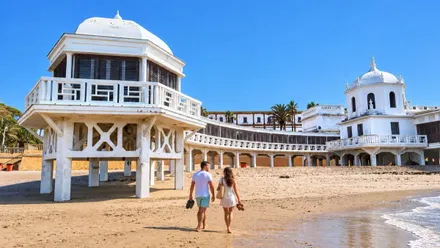 Vista del Balneario de La Palma en Cádiz con una pareja caminando por la orilla, en la playa.