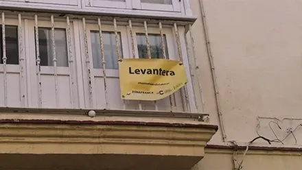 Balcón acristalado de una vivienda de Cádiz, con barandilla blanca, en la que cuelga un cartel amarillo con la palabra «Levantera» en grandes letras negras de los que reparti´´o la Zona Franca la APC en el Congreso de la Lengua de 2023.