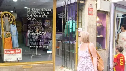 Varias personas pasan junto al escaparate de La Chula, en los Callejones de Cardoso de Cádiz, donde grandes mensajes manuscritos sobre el cristal anuncian la liquidación por cierre de la tienda.