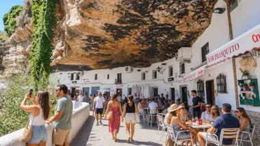 Personas paseando por la zona más turística de Setenil de las Bodegas, lucen ropas veraniegas.