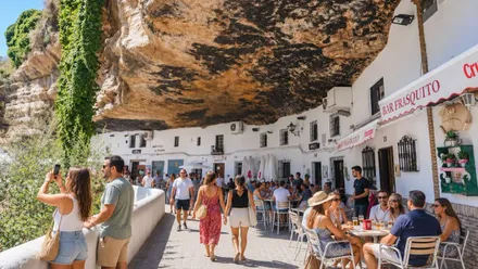 Personas paseando por la zona más turística de Setenil de las Bodegas, lucen ropas veraniegas.