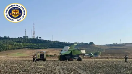 Bomberos en medio de un campo junto a una cosechadora.