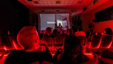 Sala de cine en tonos rojos con personas viendo un cortometraje.