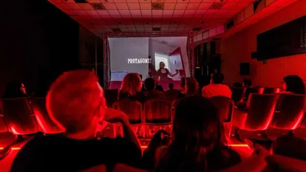 Sala de cine en tonos rojos con personas viendo un cortometraje.