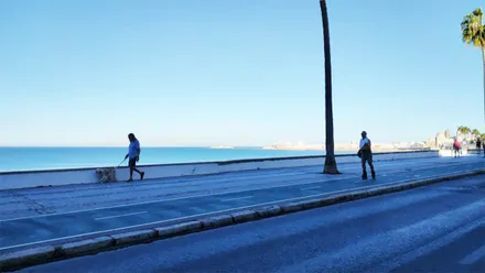 Un hombre patina por el paseo marítimo junto a la playa de Santa María del Mar, con el mar en calma y el cielo completamente despejado al fondo.