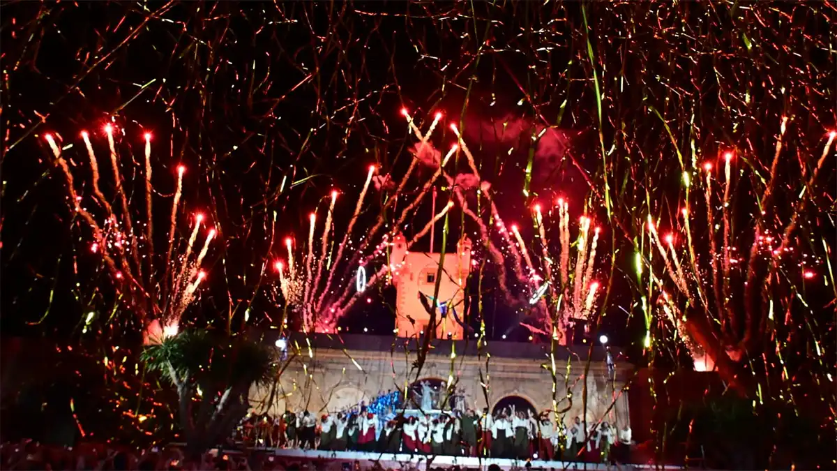 Fuegos y serpentinas cubren el cielo sobre la Puerta de Tierra durante el espectáculo de clausura de Emporio del Orbe, con numerosos artistas sobre el escenario.