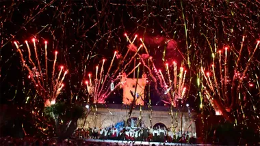 Fuegos y serpentinas cubren el cielo sobre la Puerta de Tierra durante el espectáculo de clausura de Emporio del Orbe, con numerosos artistas sobre el escenario.