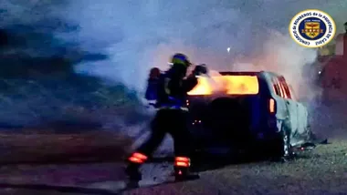 Imagen nocturna de un bombero apagando las llamas en un coche.