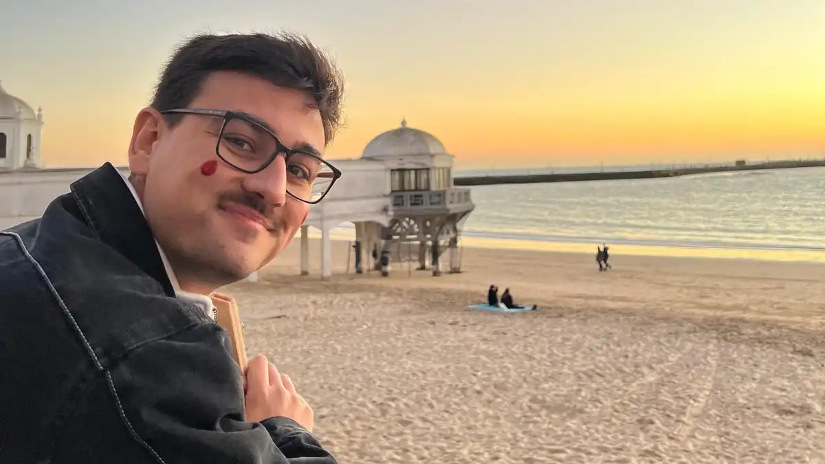José David Manjón-Cabeza Cantero posa junto a la playa de La Caleta de Cádiz al atardecer, con el antiguo Balneario de Nuestra Señora de la Palma al fondo.