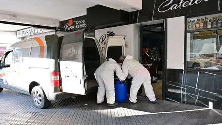 Dos operarios con epi blanco cargando un bidón azul con comida en mal estado.