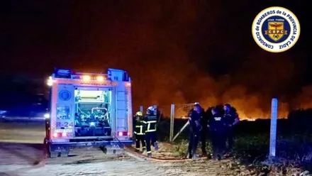 Monte bajo ardiendo y bomberos junto a un vehículo para sofocar las llamas.
