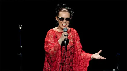 Martirio canta con un micrófono en la mano durante un concierto, vestida de rojo y con sus tradicionales gafas oscuras.