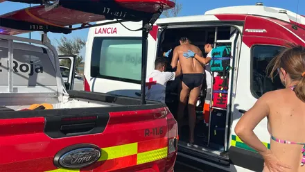 Un bañista, vestido con un bañador negro, entra asistido por personal de Cruz Roja en un vehículo de emergencias tras su rescate en Sancti Petri. En primer plano se observa otro vehículo de Cruz Roja utilizado en el operativo.