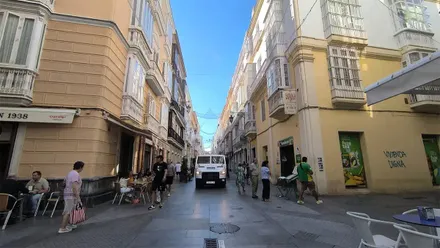Calle Ancha de Cádiz bajo un cielo azul, con varias personas y un vehículo por ella