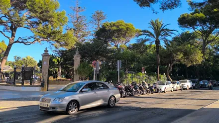 Un vehículo detenido en el semáforo que se encuentra en la entrada del parque Genovés de Cádiz. Los árboles y banderas de la avenida demuestran la presencia de Levante