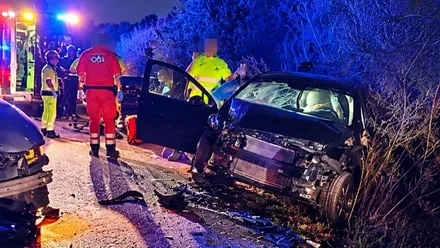 Coche accidentado con la parte delantera muy dañada, hay miembros de Urgencias y Bomberos. Es de noche, destacan las luces azules.