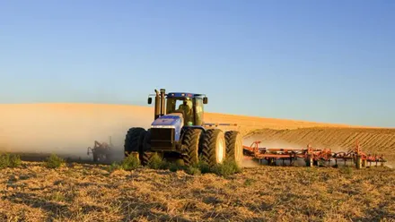 Tractor agrícola trabajando sobre un terreno de cultivo en Andalucía, con campos de labor alrededor.