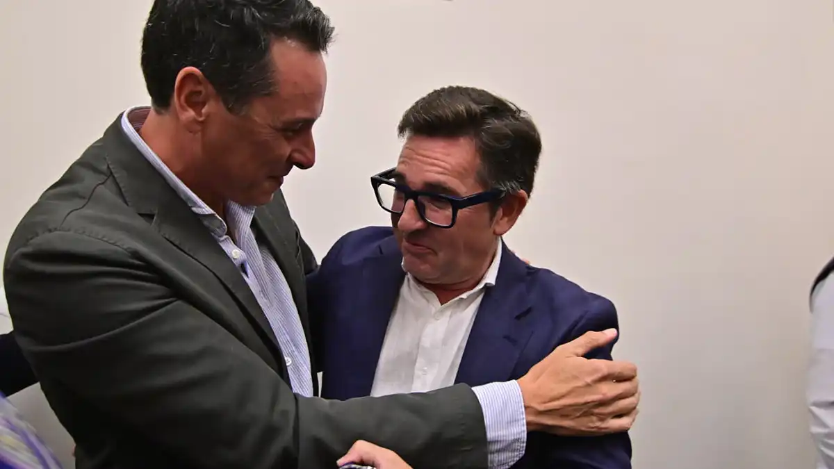 Antonio García Sánchez, con chaqueta oscura, recibe la felicitación de Isidoro Cárdeno hijo, que le abraza durante el acto de elección del Cortejo Real de Cádiz de 2027.