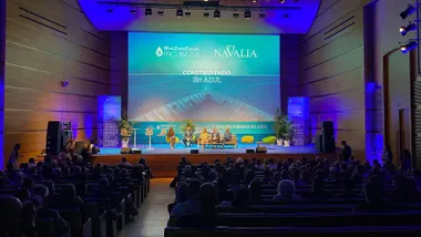 Vista general del auditorio del Palacio de Congresos de Cádiz, con numerosas personas sentadas frente a un escenario iluminado en tonos azules. Sobre el escenario intervienen varios participantes y una gran pantalla muestra los logotipos de Blue Zone Forum y Navalia junto al lema 'Construyendo en azul'.