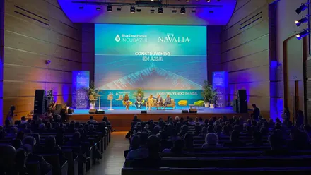 Vista general del auditorio del Palacio de Congresos de Cádiz, con numerosas personas sentadas frente a un escenario iluminado en tonos azules. Sobre el escenario intervienen varios participantes y una gran pantalla muestra los logotipos de Blue Zone Forum y Navalia junto al lema 'Construyendo en azul'.