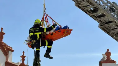 Un bombero rescata a un trabajador, en una camilla naranja, de una azotea en San Fernando.