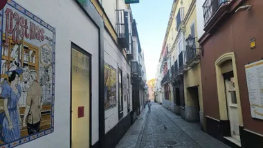 Imagen de la calle Ceballos con el mural de azulejos de la Farmacia del Mentidero en primer término y un cielo azul al fondo sobre el Gran Teatro Falla