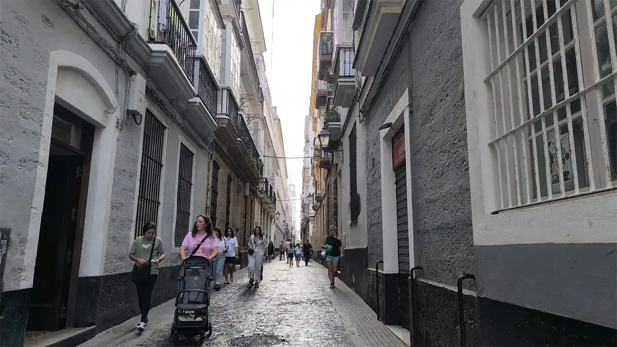 Vista de la calle Sacramento de Cádiz, con edificios residenciales a ambos lados y varias personas caminando por la vía.