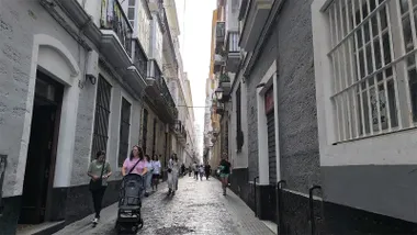 Vista de la calle Sacramento de Cádiz, con edificios residenciales a ambos lados y varias personas caminando por la vía.