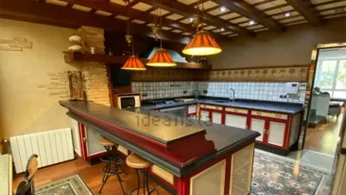 Amplia cocina de la vivienda con una gran barra central, muebles en tonos rojos y crema, lámparas colgantes, vigas de madera y suelos con motivos geométricos.