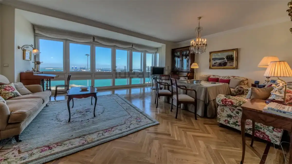 Amplio salón con zona de estar y comedor y una gran fachada acristalada desde la que se contempla el puerto de Cádiz.