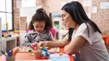 Profesora con una niña en clase haciendo manualidades.