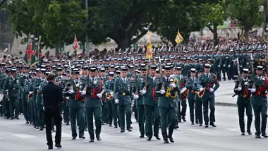 Amplia formación de guardias civiles bajando por la Cuesta de las Calesas hacia la plaza de Sevilla y la Avenida del Puerto de Cádiz, con mandos y enseñas al frente y numeroso público al fondo.