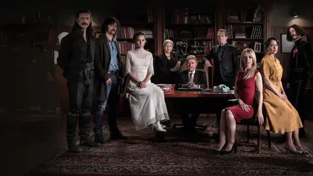 El reparto de El Ministerio del Tiempo posa caracterizado en un despacho con estanterías de libros, alrededor de una mesa de madera.