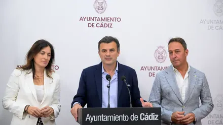 Ana Sanjuán, concejala de Vivienda, a la izquierda; el alcalde Bruno García, en el centro, hablando ante dos micrófonos; y José Manuel Cossi, responsable de Urbanismo, a la derecha, durante una comparecencia en el Ayuntamiento de Cádiz.
