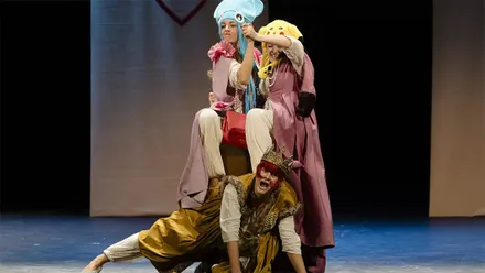 Las tres intérpretes de Las Niñas de Cádiz sobre el escenario del Teatro Falla. Dos llevan vestidos rosas y llamativos tocados de animales, mientras una tercera, con corona y vestuario dorado, aparece en el suelo a cuatro patas y con la boca abierta.