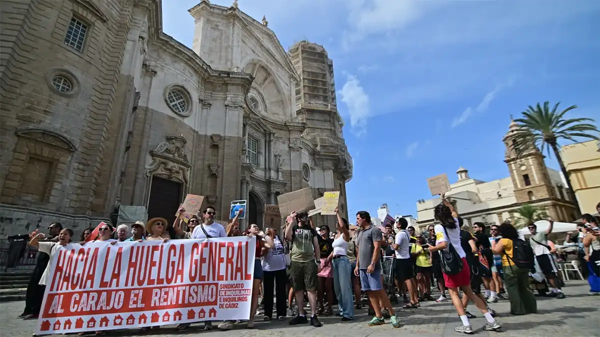 Manifestantes ante la Catedral de Cádiz sostienen una pancarta con el lema "Hacia la huelga general. Al carajo el rentismo".