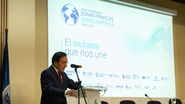 José Manuel Albares, vestido con traje oscuro y corbata roja, interviene ante un micrófono desde un atril. Detrás de él, una gran pantalla muestra el logotipo de la XXIX Conferencia de Zonas Francas Iberoamericanas Cádiz 2026 y el lema "El océano que nos une".