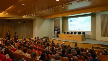 Vista general de un auditorio con numerosas personas sentadas en butacas rojas y naranjas. Al fondo, José Manuel Albares interviene desde un atril junto a varias banderas. Detrás aparece una gran pantalla con el logotipo de la XXIX Conferencia de Zonas Francas Iberoamericanas y el lema «El océano que nos une».