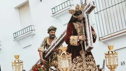 Jesús Nazareno de Arcos de la Frontera porta la cruz acompañado por el Cirineo durante una salida procesional por las calles de la localidad.