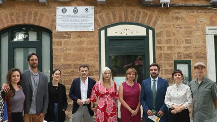 Nueve personas posan ante la fachada de la casa natal de Manuel de Falla en Cádiz, con balcones blancos, una placa conmemorativa y un farol.