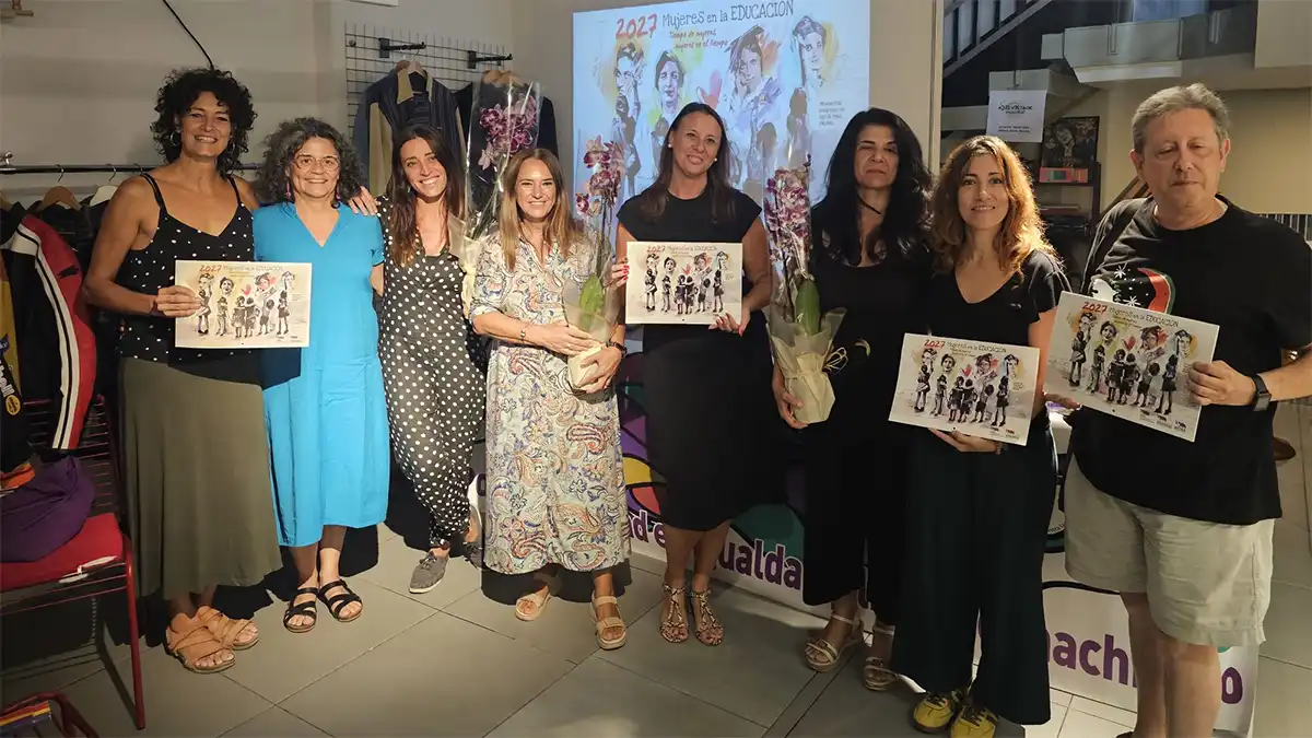 Grupo de participantes en la presentación del calendario coeducativo de 2027 en Cádiz, varias de ellas sosteniendo ejemplares de la publicación, con una proyección sobre mujeres en la educación al fondo.