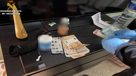 Agente de la Policía Nacional contando dinero con pastillas y droga sobre la mesa.