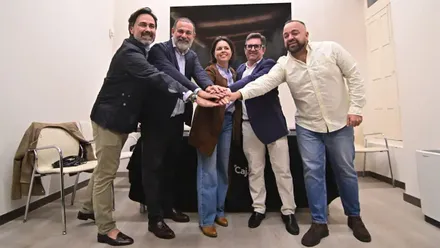 Cinco personas elegidas para integrar el Cortejo Real de Cádiz de 2027 posan juntas y colocan sus manos unas sobre otras.
